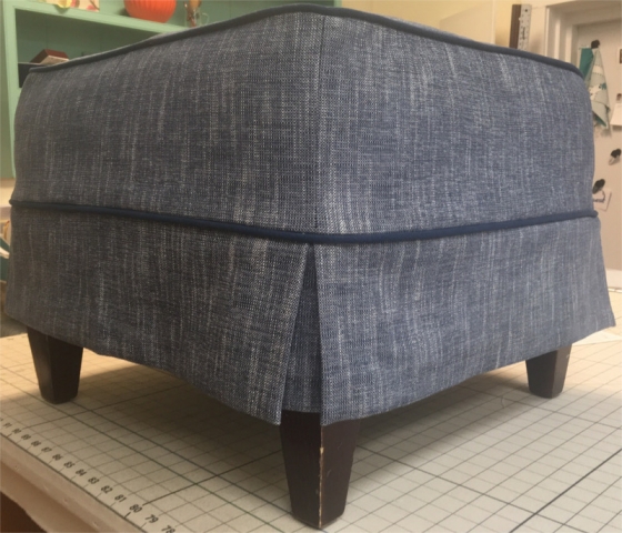Footstool covered with grey textured fabric and piping accent