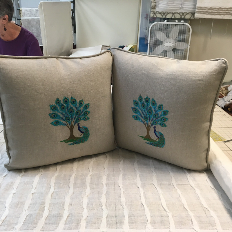 Two matching throw pillows with centered peacock pattern and piped edging