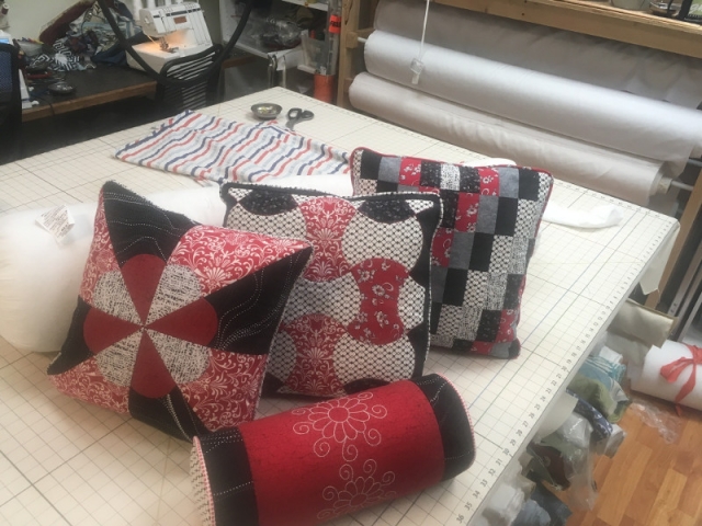 Three quilt-patterned throw pillows of mixed fabrics and matching small bolster