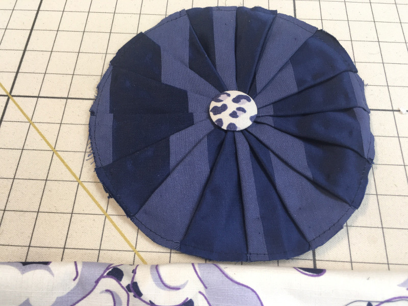 Round pleated fabric with button center on work board, work in process
