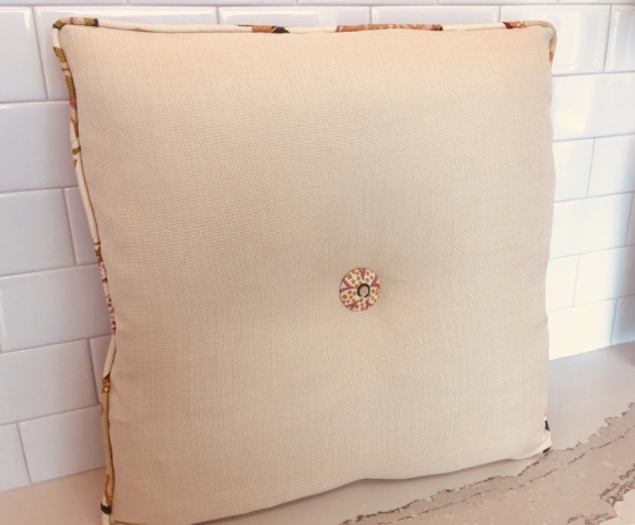 Square throw pillow with piped edging and matching fabric button center