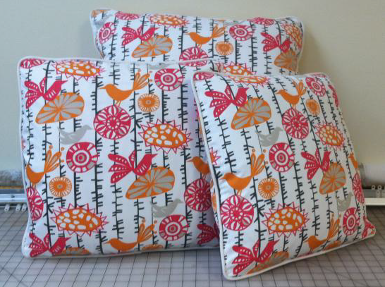 Three colorful bird and flower fabric pillows with white piping