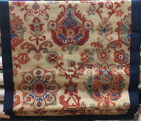 Closeup of roman shade, fabric of cream background with burnt orange, blue and soft blue flowers and border of royal blue