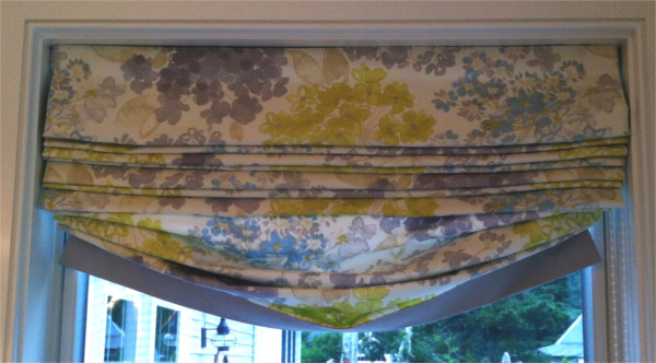 Relaxed roman shade mounted on rod above window, grey and yellow flowered print